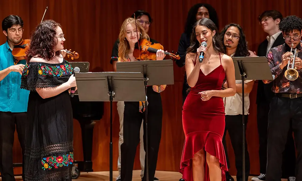 Nichole Waligóra singing on stage, surrounded by other musicians playing violins, trumpets, and other instruments.